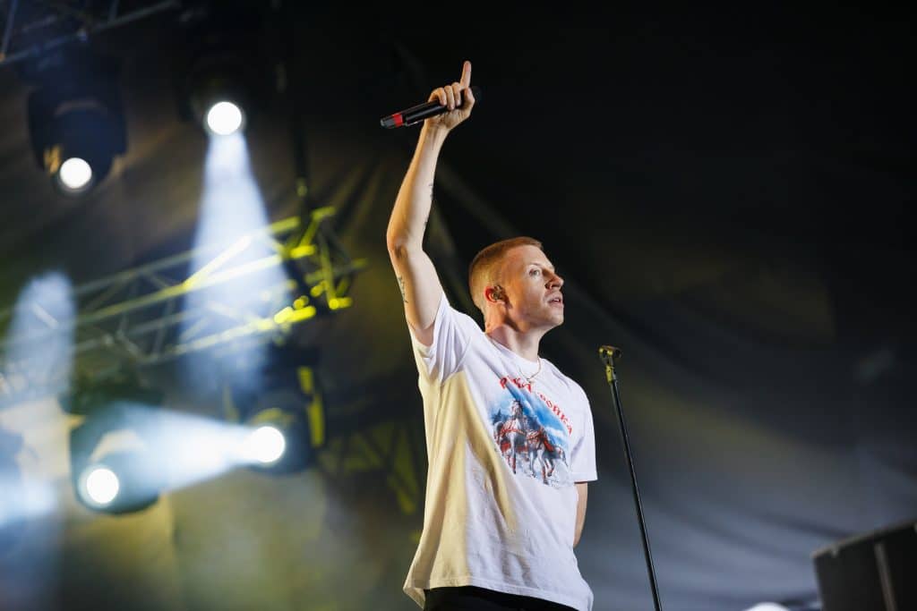 Macklemore performing on stage in a white t-shirt.