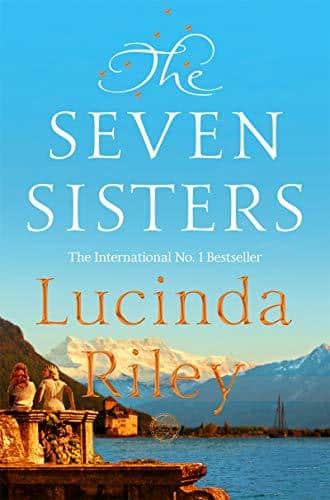 photo of a book cover: a big blue sky rising from some mountains, in the foreground are two women sitting on a stone balcony looking out onto the lake at the foot of the mountains. The title is at the top centre of the title in whispy white writing, and below in the same whispy writing but gold, is the authors name