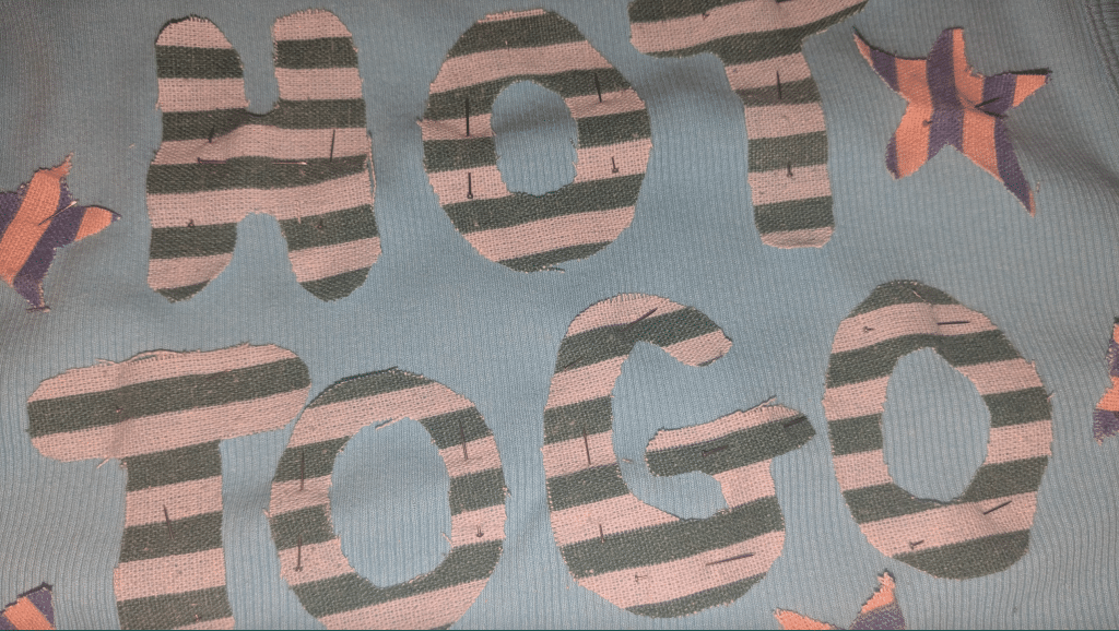 Image of the fabric spelling hot to ho pinned onto a blue tank top