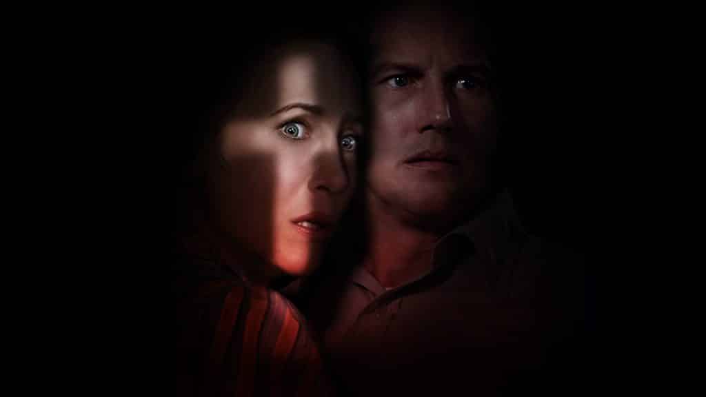 Ed and Lorraine look off screen frightened, while a light in the shape of a crucifix is cast on their face.