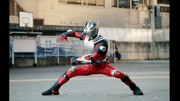 Kamen Rider Ryuki takes a fighting stance in a concrete lot.