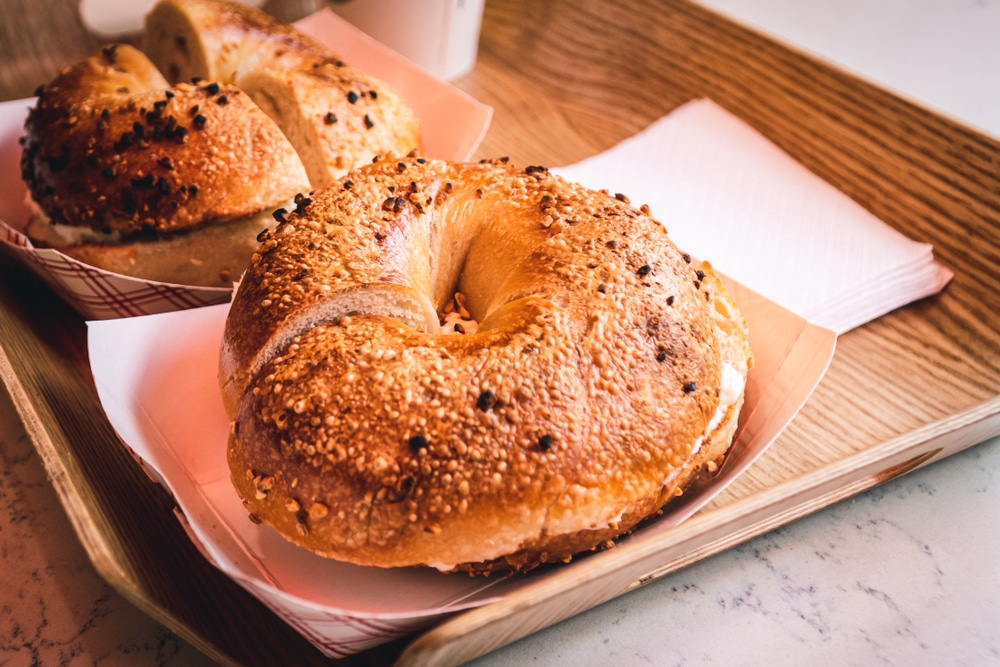 Two sesame seed bagel on a wooden tray with napkins