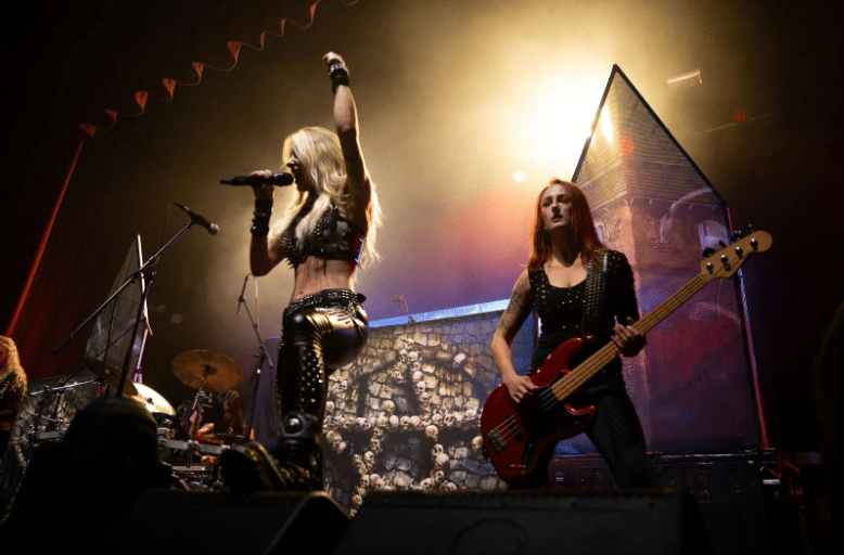 Burning Witches performing. The singer and bassist are standing next to each other.