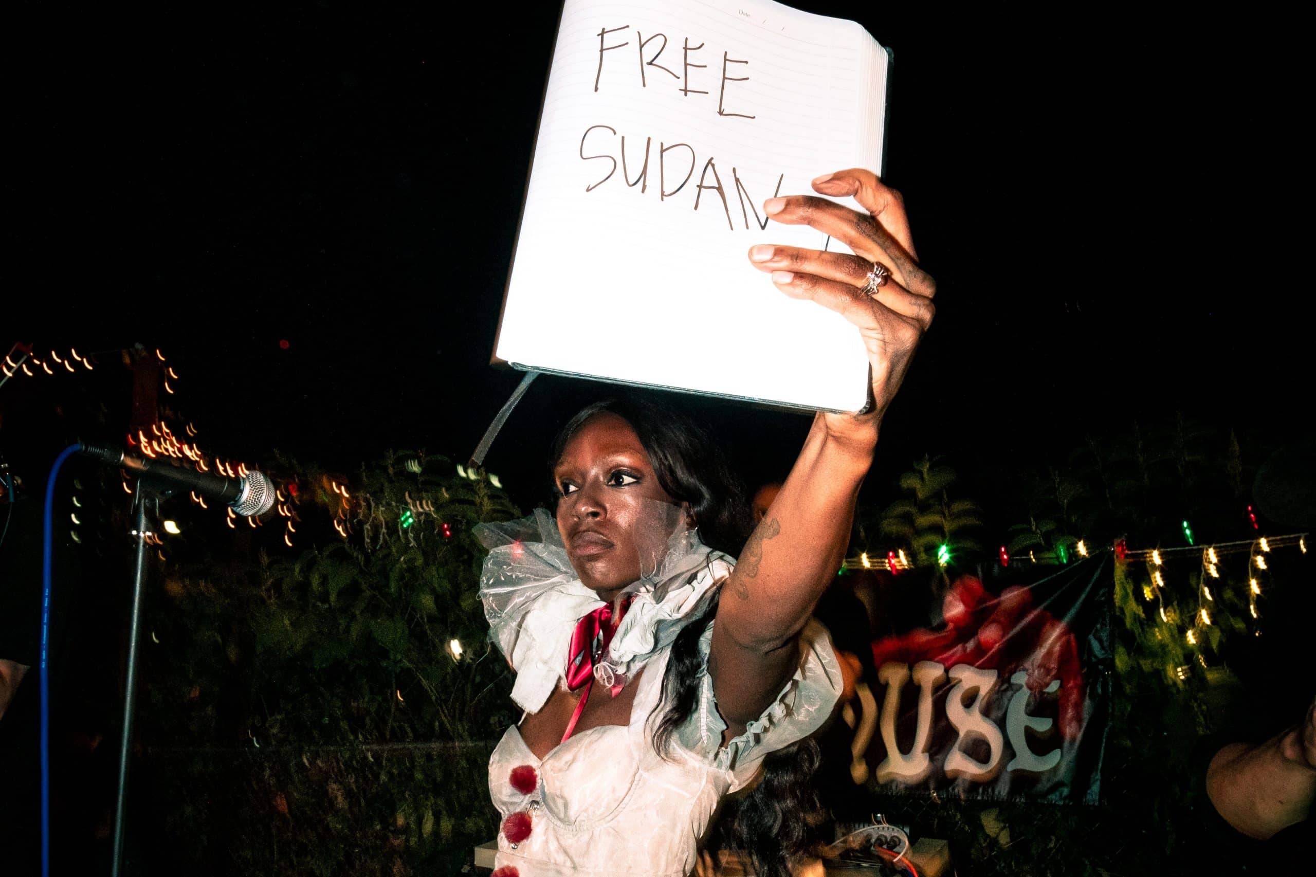 A photo of TeZaTalks holding up a sign that reads "Free Sudan" at a music show.