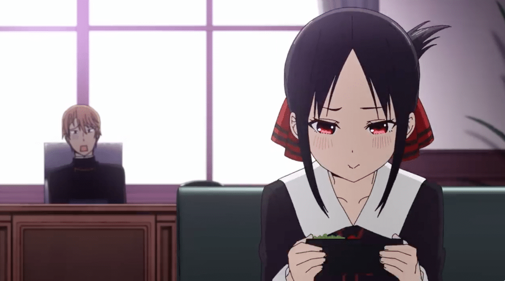 The image depicts a still from an anime. The main focus is on a young woman with long, straight black hair styled in two low pigtails. Her hair is adorned with a large, red bow. Her facial features are softly drawn, large expressive red eyes, and a slight smirk playing on her lips. She possesses a visibly fair complexion, and the light blush on her cheeks adds to the overall gentle, almost childlike innocence. She's wearing a school uniform-like outfit, consisting of a dress with a white collar and what appears to be a white blouse underneath. She is seated at a sleek, dark-colored table or desk and holds a dark rectangular container with a small amount of green food, possibly a side dish like pickles or seaweed salad. Her posture is relaxed, and her hands carefully cradle the dish, suggesting a cautious and gentle interaction with the food.
In the background, slightly out of focus, is a man with light brown hair and a somewhat paler complexion. Based on the style of his clothing—a dark, collared garment suggestive of clergy or a formal setting—his appearance carries a formal or even officious air. His expression is one of slight surprise or bewilderment, his mouth slightly agape, indicating a possible reaction to the woman's actions or demeanor. He sits at a similar desk behind the main subject, maintaining a distance that emphasizes his secondary position in the scene.
The atmosphere is calm and slightly mysterious, with a subdued color palette dominated by dark purples, blacks, and muted light shades that enhance a certain soft lighting. There's a sense of casual intimacy yet also a hint of tension or intrigue owing to the contrast in expressions between two characters. A large window with white panels and purple highlights is visible, providing subtle lighting to the scene while suggesting an indoor, possibly institutional, setting. The background is rather minimalistic, focusing the viewer's gaze directly on the main subject. Generally, the mood is quiet observation, possibly highlighting the contrast of behaviors and social dynamics between the two people, and inviting interpretation of their relationship or a developing narrative.