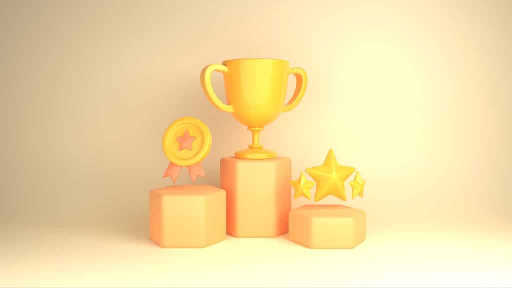 Image of first, second, and third platform awards side-by-side, descending in height. as they descend in rank First place is a trophy, the second is a metal, the third is a star, each sitting on their respective platforms. The awards are yellow, and the platforms are orange.