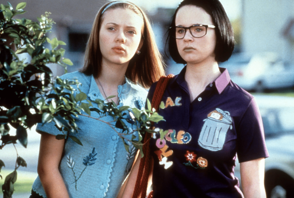 Scarlett Johansson (left) and Thora Birch (right) stand behind a bush staring at something.