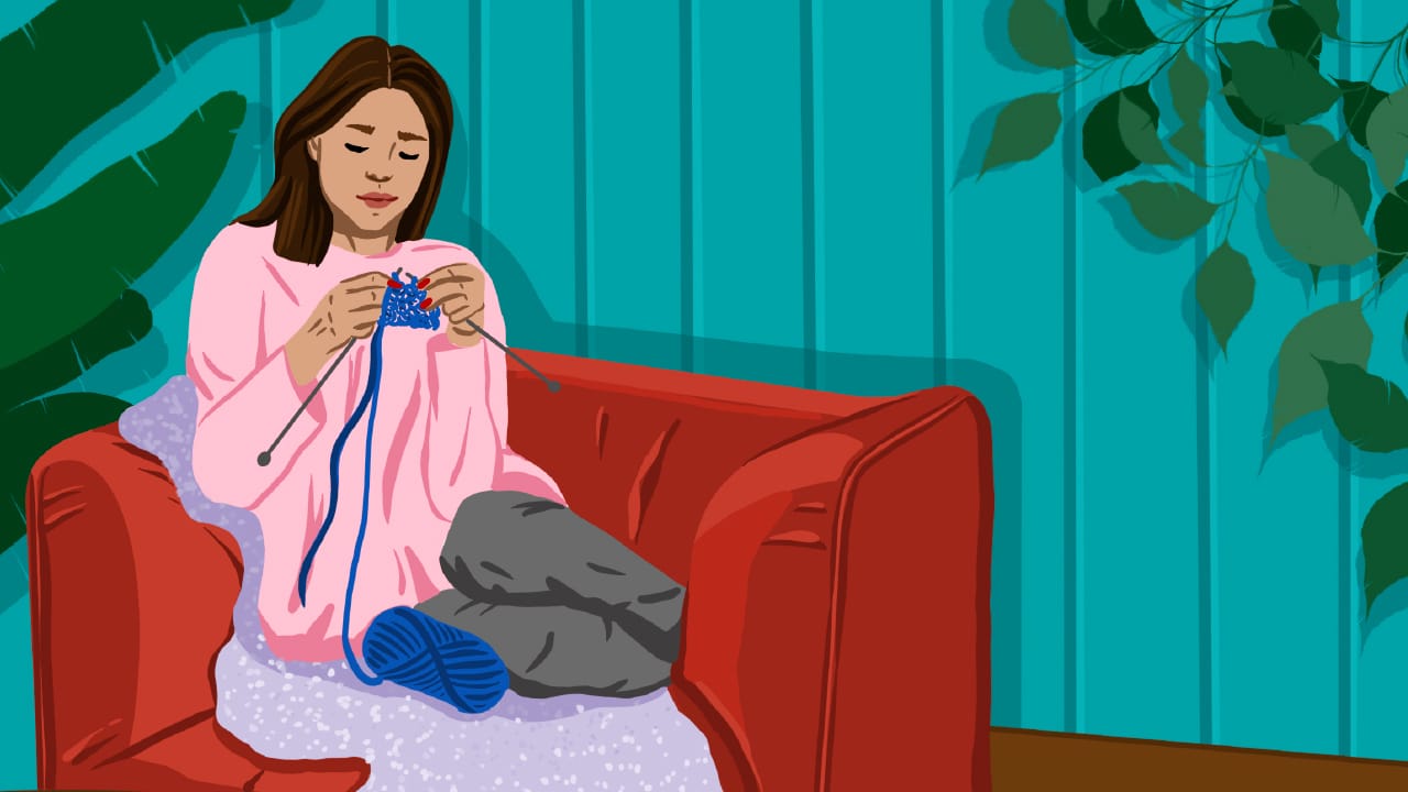 Young woman knitting on a sofa at home.