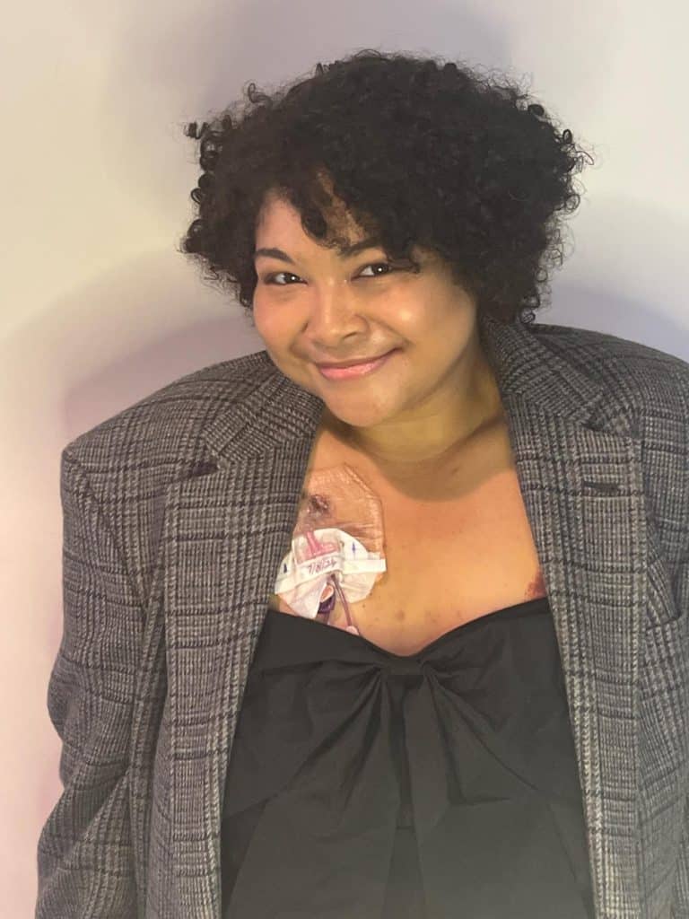 Pictured is Jade Neal, a mixed-race 26-year-old woman wearing a gray plaid vintage Burberry blazer over a black dress with a bow in the center.
