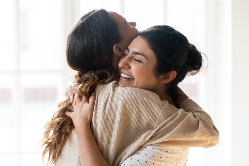 Candid, diverse girl best friends embracing, indoors, close-up