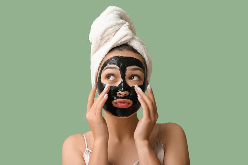 Young woman applying a charcoal face mask.