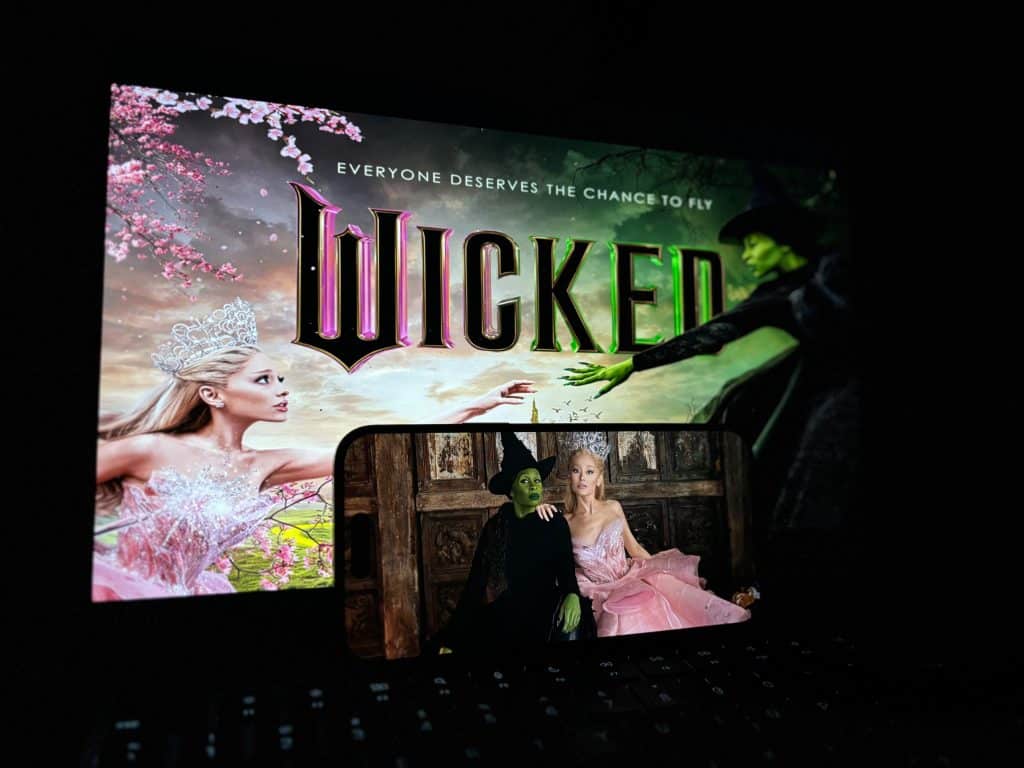 A promotional picture of the Wicked poster behind a picture of Elphaba and Glinda.