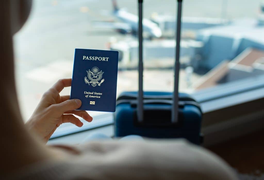 Woman holding up an American passport at an airport with luggage.