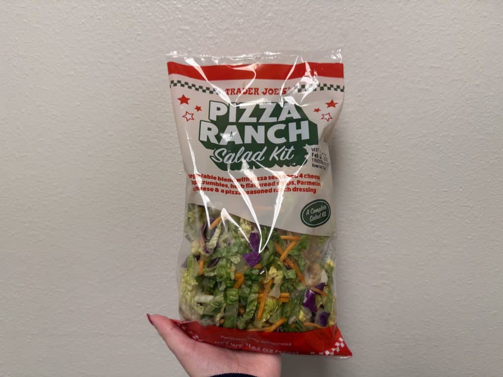 A packaged plastic bag of a salad kit in front of a white wall background