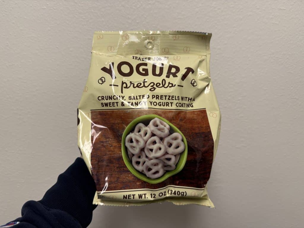A larger, maize-colored plastic bag of yogurt-covered pretzels in front of a white wall background