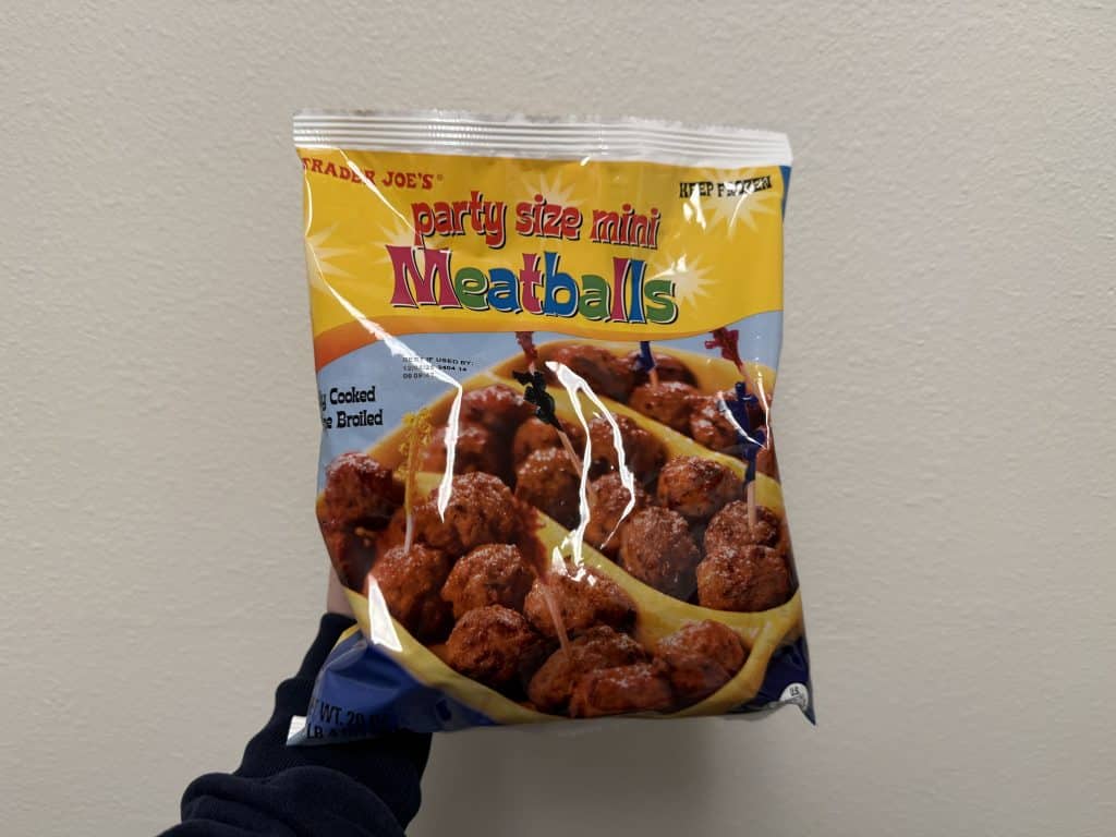 A plastic bag of party size mini meatballs in front of a white wall background. The lettering is bright and colorful.