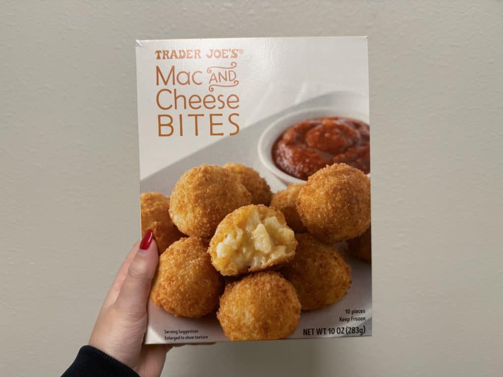 A box of frozen mac & cheese bites, with an image of mac and cheese bites with ketchup displayed on the front. Box in front of a white wall background.