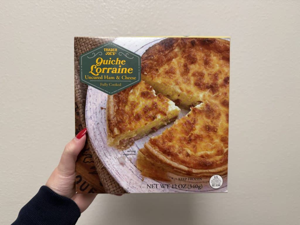 A box of a mini, frozen quiche Lorraine with an image of quiche Lorraine on the front. Box in front of a white wall background.