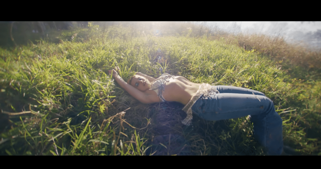 A screenshot of Addison Rae laying in a bed of grass in the "High Fashion" music video.