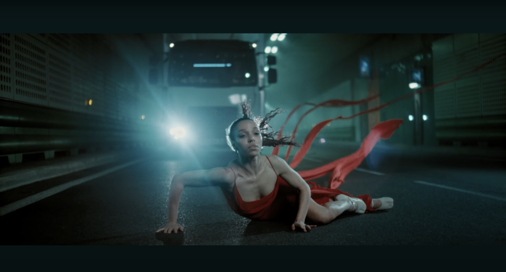 A screenshot of FKA Twigs in front of a moving truck in the "Striptease" music video.