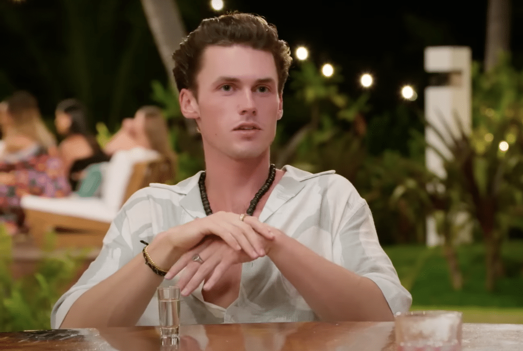 Tyler sat at a table explaining to the other islanders the new addition to their villa.