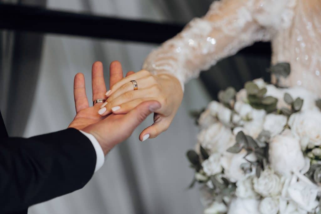 Man in suit and woman in a wedding dress holdings hands, with their arms outstretched towards each other.