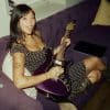 Beabadoobee laying on a couch with a purple guitar in her hands.