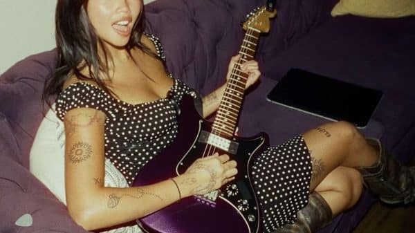 Beabadoobee laying on a couch with a purple guitar in her hands.