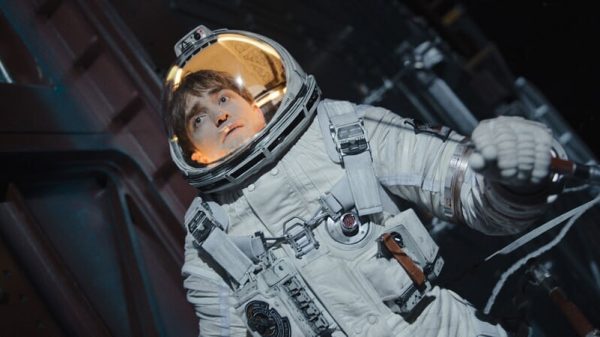A still of the film "Mickey 17" where Robert Pattinson's character wears a spacesuit and stares off into the distance.