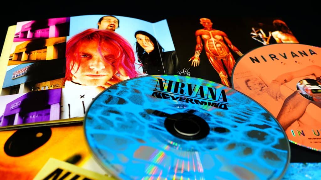An image of Nirvana CDs (Nevermind and In Utero) on top of a few various photos of the band.