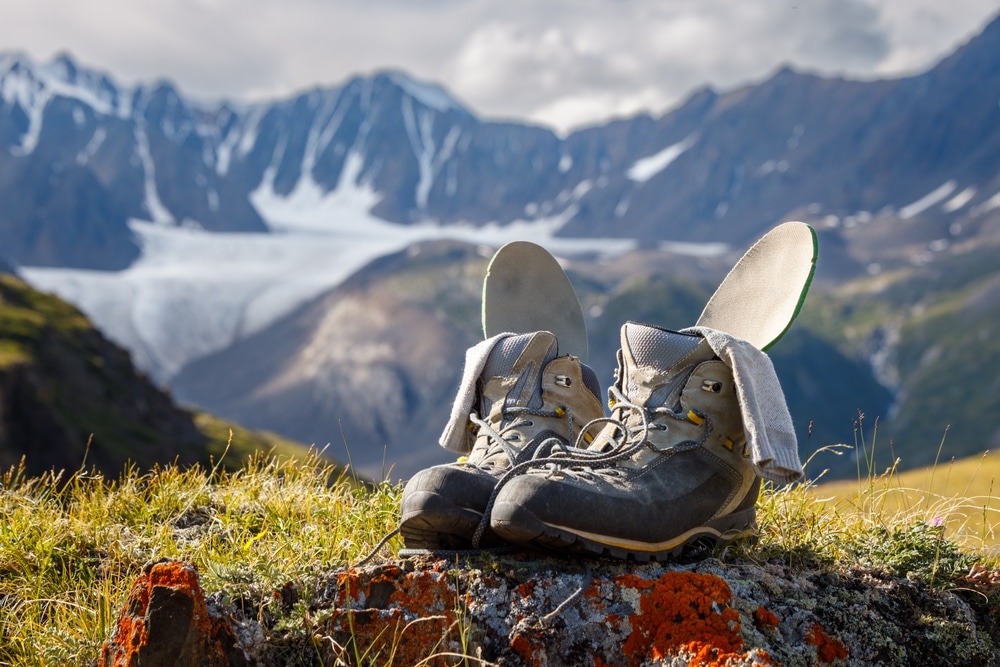 Trekking boots with insoles and socks dry on the background of a mountain valley. Boots in focus, background blurred.