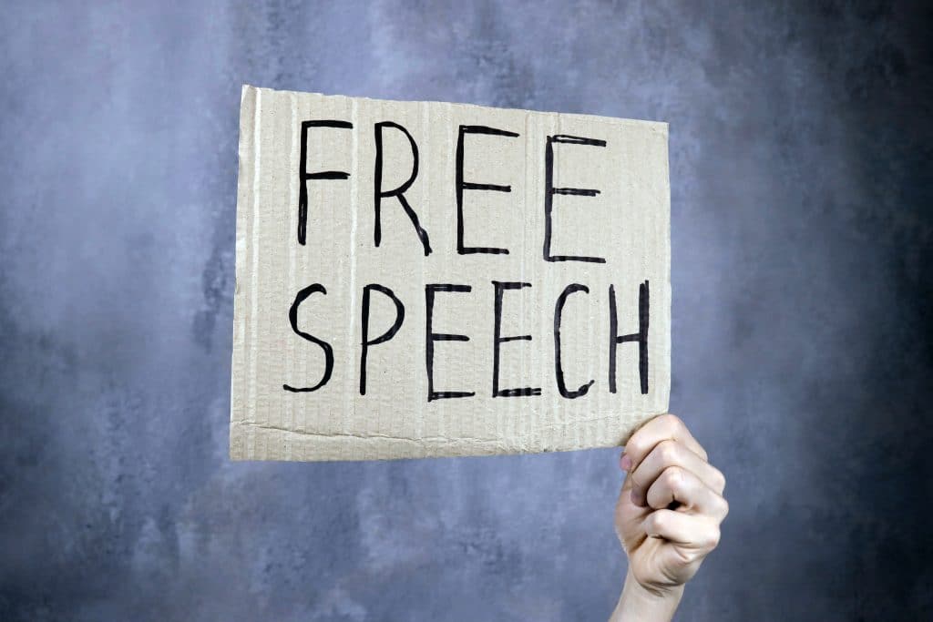 Hand holds a banner with the inscription 'free speech' written on it