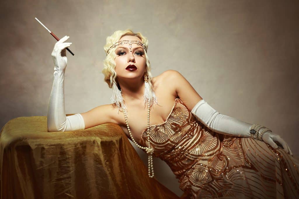 A woman dressed in 1920s fashion, posing elegantly for a photo.