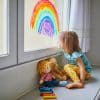 A girl sits at a window seat gazing at a rainbow