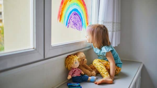 A girl sits at a window seat gazing at a rainbow