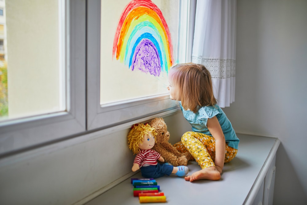 A girl sits at a window seat gazing at a rainbow