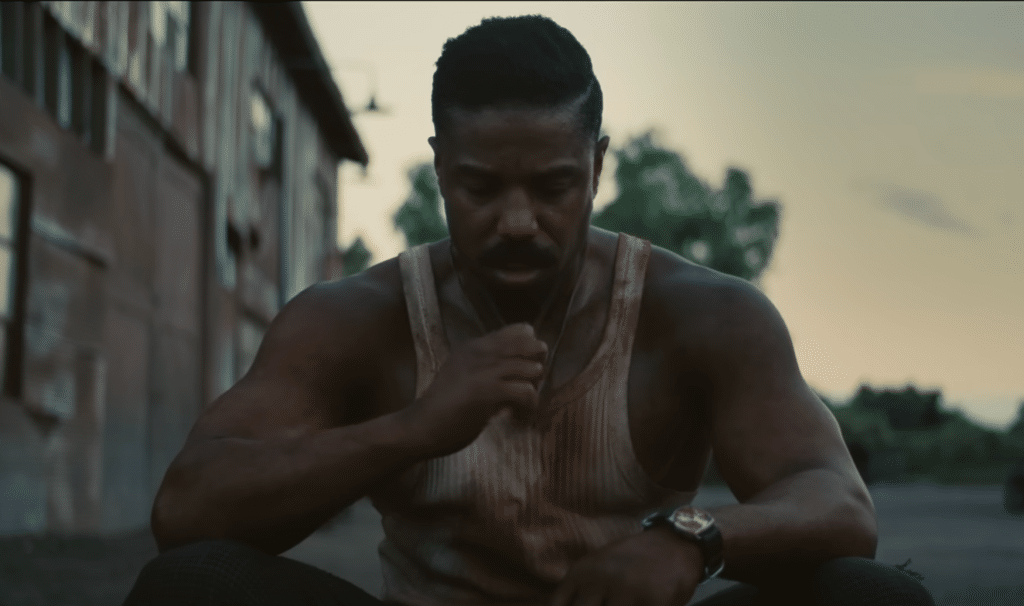 Michael. B Jordan, bloodied and looking at his cross in Sinners 2025