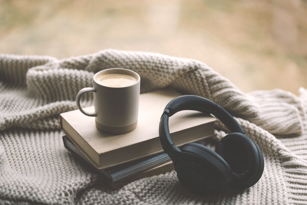 Picture of a book, coffee, and black headphones laid out on a bed