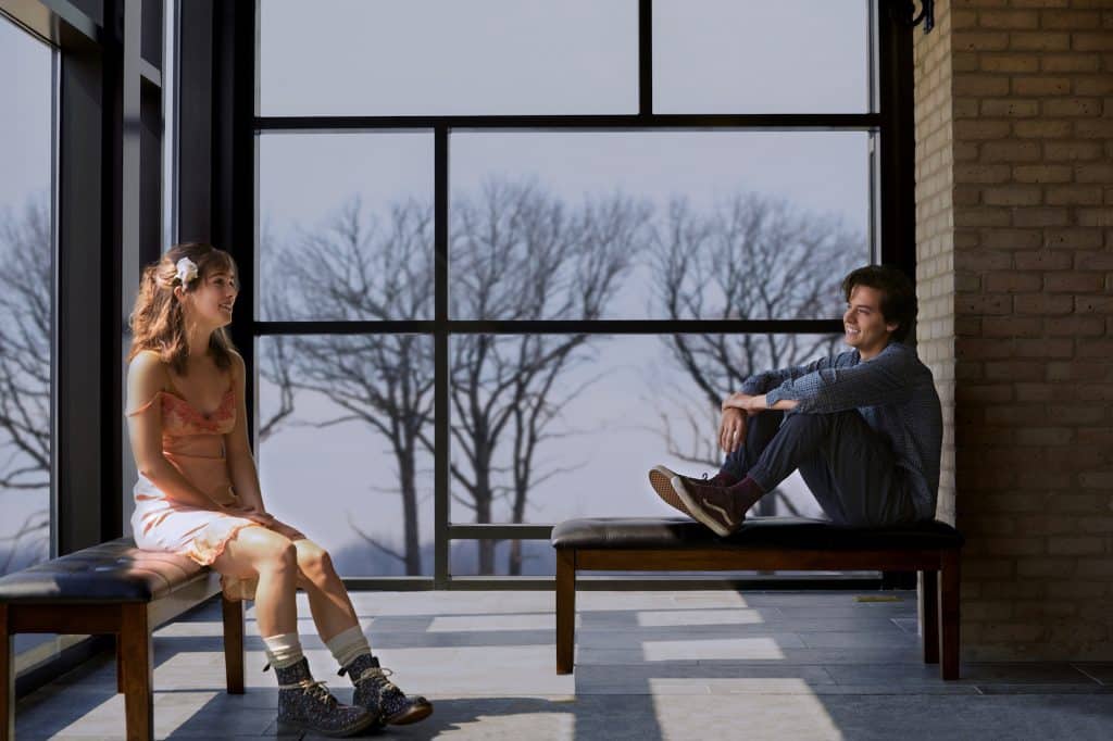 A scene from Five Feet Apart showing a woman and man sitting on benches, facing each other in a hospital setting
