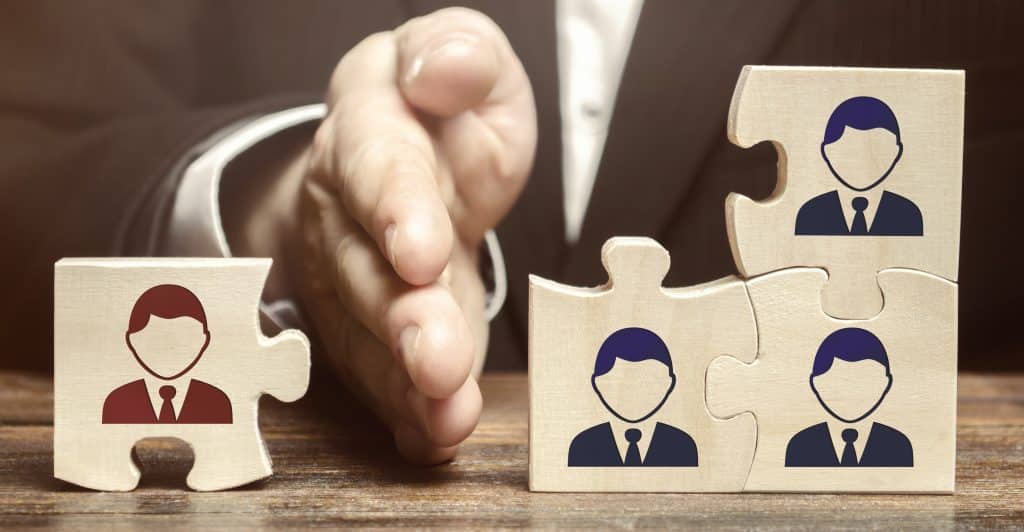 A single worker puzzle piece is separated from joining the other three worker puzzle pieces. by a large hand.