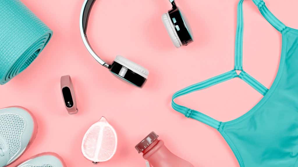Pink/coral flooring with turquoise tank top, turquoise yoga mat, headphones, fitness watch, tennis shoes, and water are sprawled out on the floor.