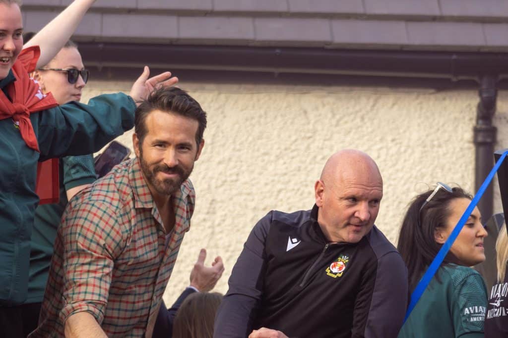 Ryan Reynolds smiles next to assistant manager Steve Parkin on the Wrexham parade bus celebrating the club's promotion.