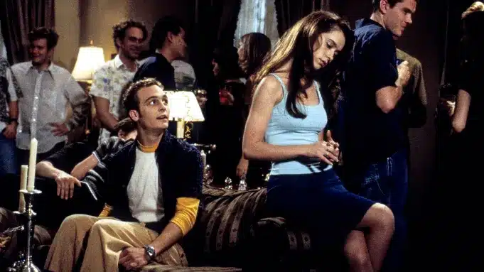 Ethan Embry on couch and Jennifer Love-Hewitt leaning against couch. Embry stares at an unphased Jennifer in adoration.