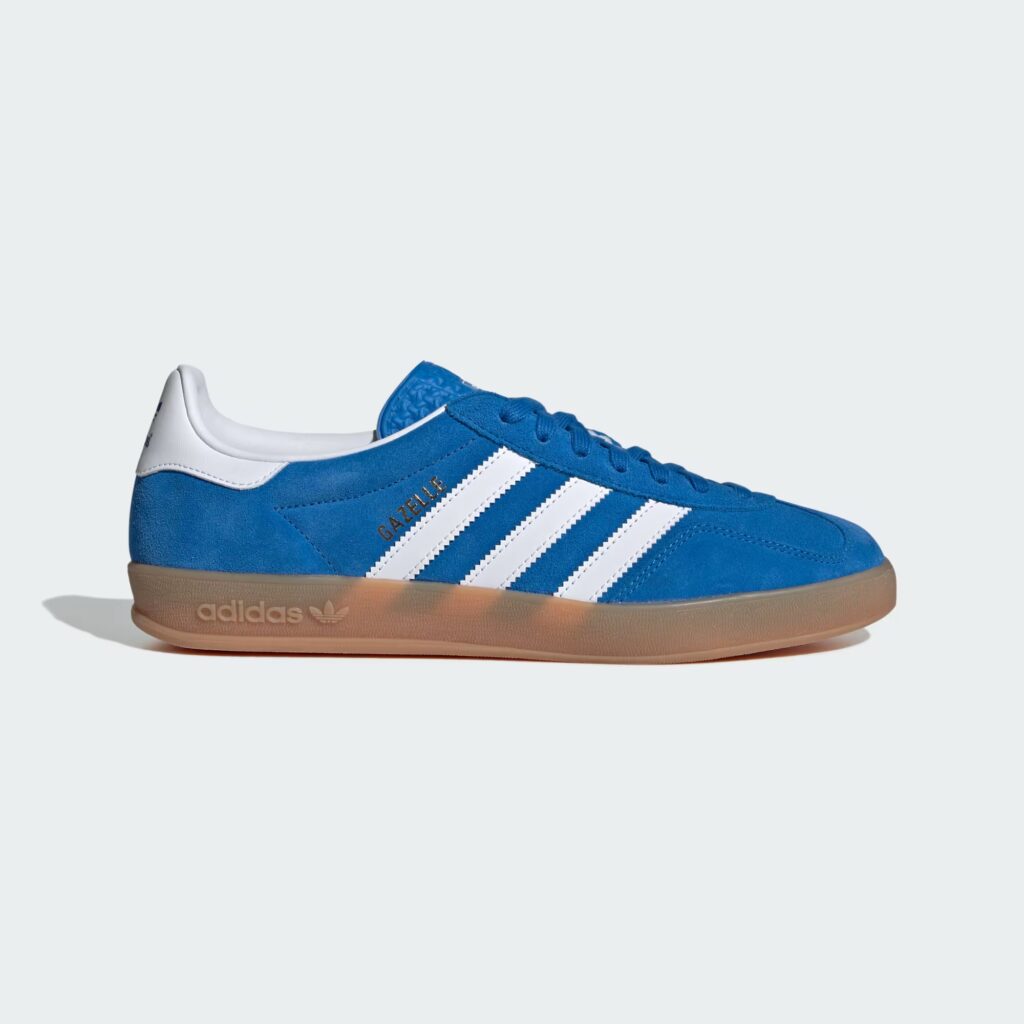 Adidas Gazelles in a blue color way, features a gum sole, blue upper, white three stipe Adidas branding, and blue shoe laces.