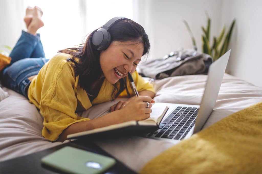 Girl with headphones lying on bed while happily journaling