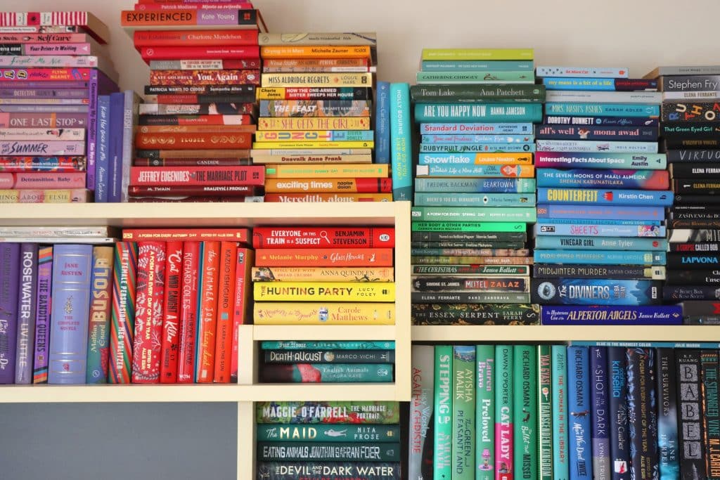 An aesthetic bookshelf full of books we buy but never read. A vibrant bookshelf filled with an array of colourful books.
