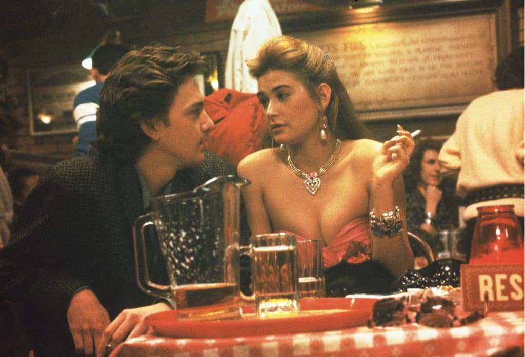 Andrew McCarthy and Demi Moore sit at a table in a bar, smoking cigarettes and drinking. They stare into each other's eyes.
