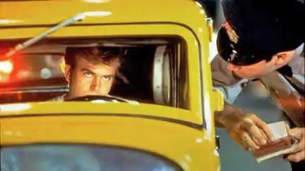 Paul Le Mat sits in a yellow car after being pulled over by a cop. The cop stands inthe window asking questions.