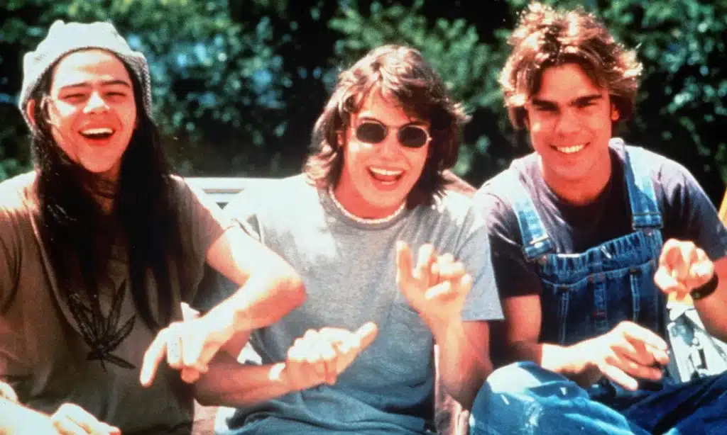 From left to right: Rory Cochrane, Jason London, and Sasha Jenson sit side-by-side on the hood of a car, laughing.