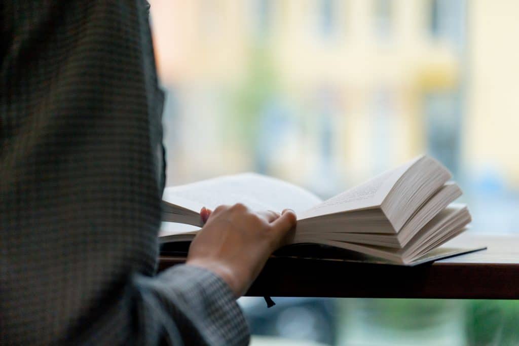 A close-up of a person's hand holding an open book, with only the hand and pages visible.
